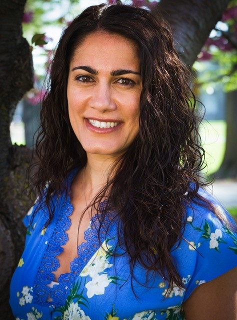 Dr. Regina Ginzburg professional head shot, wearing a floral blue top and outside background